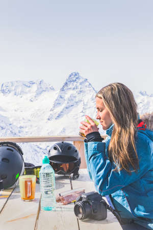 Woman drinking warm tea in the rustic wooden outdoor cafe mountain summit. Tourist lifestyle adventure concept. Alpine view, snow on hills. Active vacations Travel sport outdoor.の写真素材