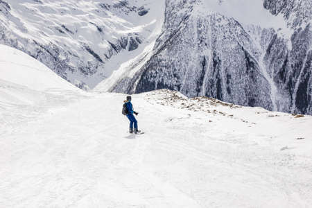 Woman snowboarder rides downhill on slope winter on a background of high mountains. Travel Lifestyle recreation and extreme concept, activities outdoors adventure vacations. View landscape ski resortの写真素材