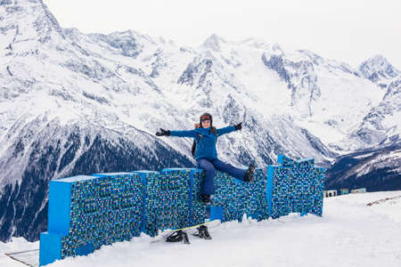 Positive girl snowboarder rejoices while relaxing in high mountains. Lifestyle winter recreation and extreme adventure concept, activities vacations outdoor. Happy woman during vacation at ski resort.の写真素材