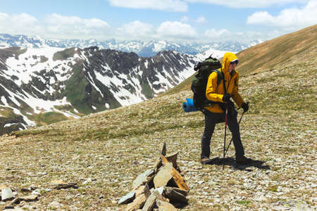 Tourist climber in sports outfit with backpack and sticks climbs to top of mountain against backdrop of snow-capped mountain ranges. Landscape Travel Lifestyle Concept travel to remote places planet.の写真素材