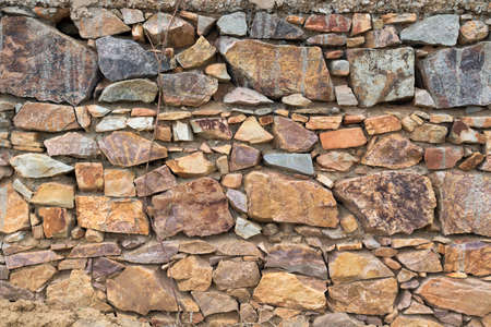 Wall texture background stone. Grunge facing coarse, rough stone or rock texture of mountains. Grungy aged stonework city. Damage front decor house.の写真素材