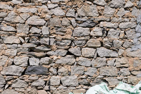 Grunge texture stone wall background. Rough old stone or rock texture of mountains. Coarse facing, grungy aged stonework city. Front antique decor house. General layout of stone masonry.の写真素材