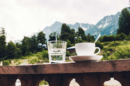 Cup of tea and a glass of water on a terrace on the porch curb against the backdrop of a picturesque viewの写真素材