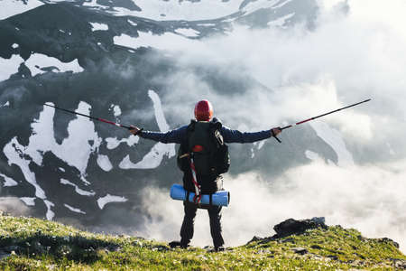 Happy tourist with large backpack and sticks climbed to top of mountain and rejoices at achieved...