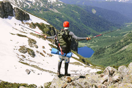Man adventurer on mountain summit hiking Traveling alone with large backpack climbed the top of high snow-covered rocks and valleys with a lake. lifestyle concept active weekend vacations wild natureの写真素材