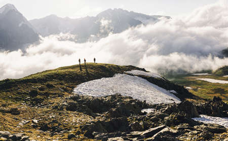 Tourists are standing on top of snowy hill admiring the stunning view of white clouds against the backdrop of high rocks on sunny warm spring day. Concept of journey to far corners of the planetの写真素材