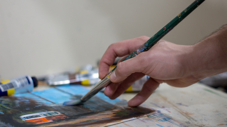 Closeup of man's hand holding a paintbrush-  creating an acrylic or oil painting on canvas panelの写真素材