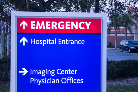 close up Red and blue emergency center sign with hospital entrance in background