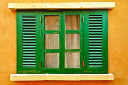 Closed green window shutters on yellow house facade. の写真素材
