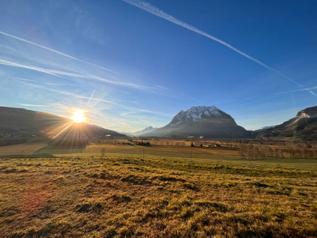 mountain landscape with blue sky, clouds, green fields and sunの写真素材