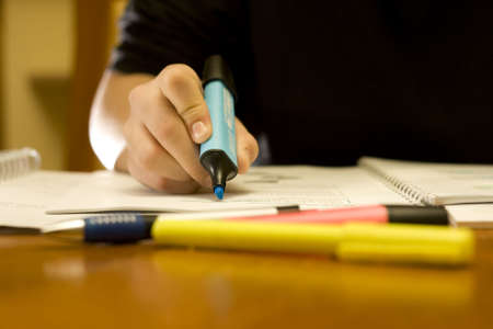 Student studying in a library using a blue marker to mark important notes.の写真素材