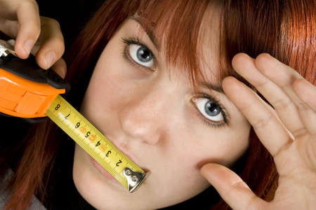 Beautiful redhead girl with blue eyes with a measuring ruler meter tape on her mouth.Studio shot.の写真素材