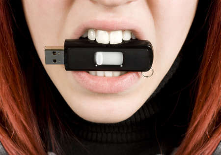 Close-up of a redhead girl nervously biting an usb flash drive stick.Studio shot.