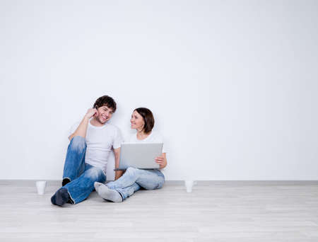 Beautiful smiling couple relax in the empty room with laptop  - new home