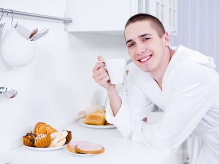 Portrait of handsome smiling young man with cup in the kitchenの写真素材