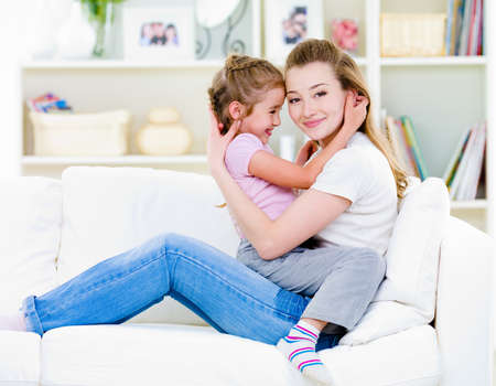 Happy mother with litttle daughter sitting togather on the sofa at homeの写真素材