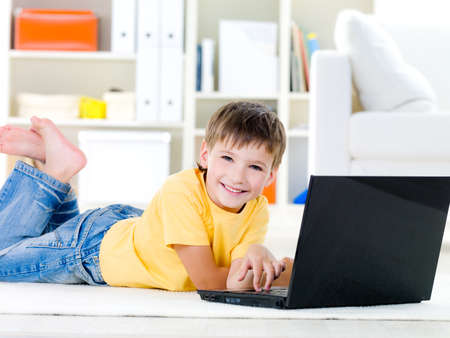 Happy little boy with laptop lying on the floor at home - indoorsの写真素材