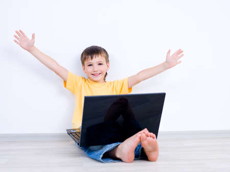 Happy little boy with laptop with moving apart his hands - indoorsの写真素材
