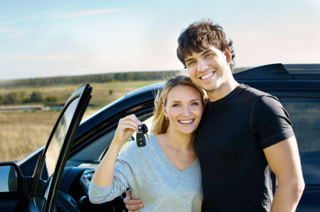 portrait of happy bautiful couple showingh the keys standing near the car の写真素材