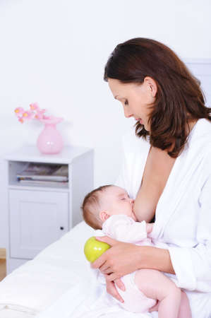 Mother breastfeeding her newborn child and holding green apple - indoors
