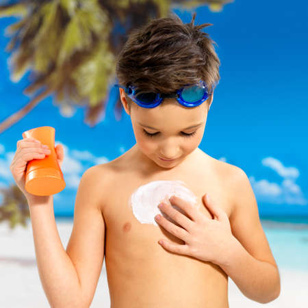 Schoolchild boy applying sun block cream on the tanned body.  Boy holding orange sun tan lotion bottle.の写真素材
