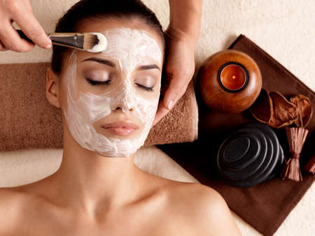 Spa therapy for young woman receiving facial mask at beauty salon - indoorsの写真素材