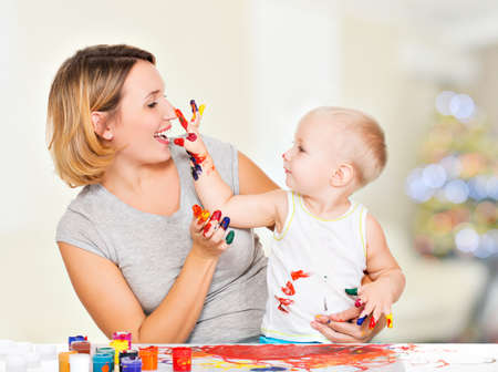 Happy child draws on the face of his mother -  at home.の写真素材