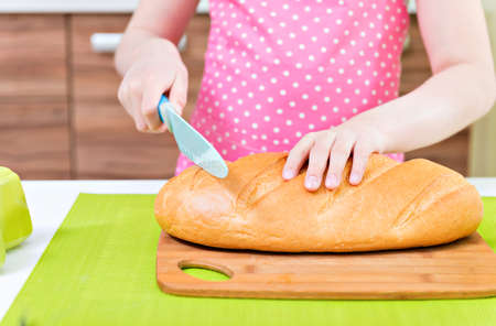 Happy little girl in pink apron cutting bread in the kitchen.の写真素材