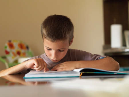 Portrait of focused boy reading a book while sitting at table at home.の写真素材