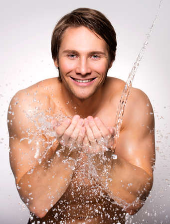 Portrait of a handsome smiling man washing his healthy face with water on gray background.の写真素材