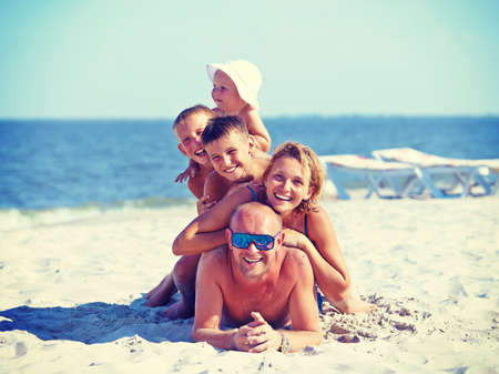 Happy mother and father with three children lying on the sunny beach.の写真素材