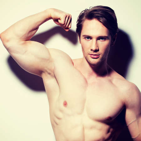 Portrait of a sexy muscular young man posing on a white background with contrast shadows.
