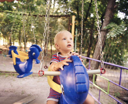 Little blond boy on a swing in a summer park.の写真素材