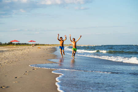 Two happy boys running on the sea beach at summer with raised armsの写真素材