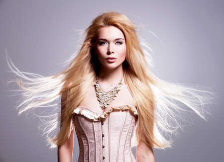 Portrait of the beautiful sexy woman with long blonde hair. Fashion model posing in the studio on a black background with flying hair.の写真素材