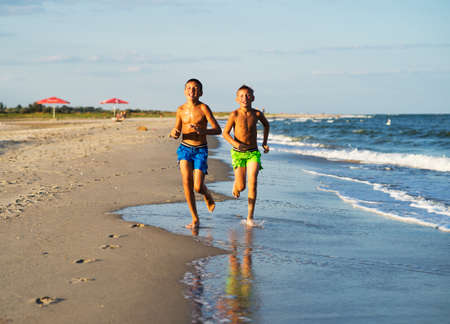 Two happy boys running on the sea beach at summer with raised armsの写真素材
