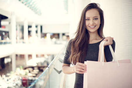 Happy beautiful woman with shopping bags stands at shop. Attractive caucasian girl with purchasing bags in big mallの写真素材