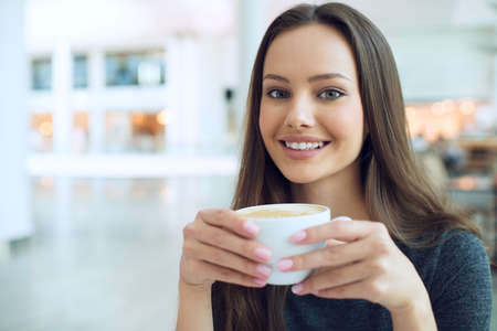 Smiling woman drinking coffee in the morning at restaurant soft focus. Closeup portrait of a pretty...
