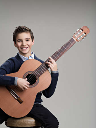 Happy boy playing on acoustic guitar. Teenager boy with classic wooden guitarの写真素材
