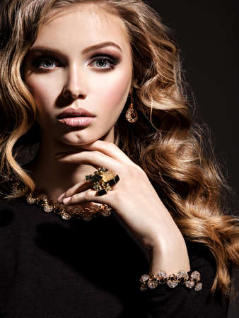 Beautiful woman with long curly hair and gold jewelry posing at studioの写真素材
