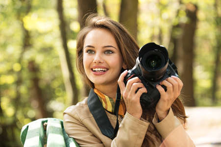 woman is a professional photographer with photo camera outdoor. Young girl taking photo outdoors with digital cameraの写真素材
