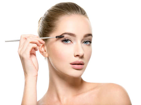 Girl makes makeup. Beautiful woman apply mascara on eyelashes  with cosmetic brush - isolated on whiteの写真素材