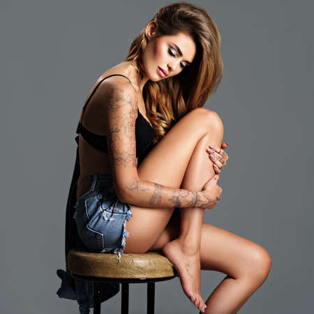 Beautiful  woman in jeans clothes with a tattoo on the body. Portrait of young adult sexy woman with brown hair. Pretty female with a half nude body.の写真素材