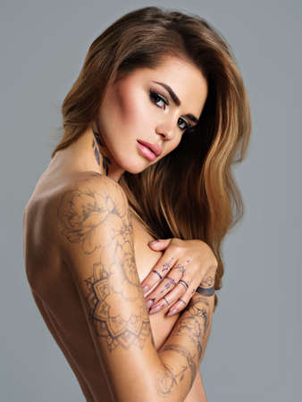 Beautiful sexy girl with a tattoo on the body. Portrait of young adult woman girl with brown hair. Sexy female with nude body and covers breast with armsの写真素材