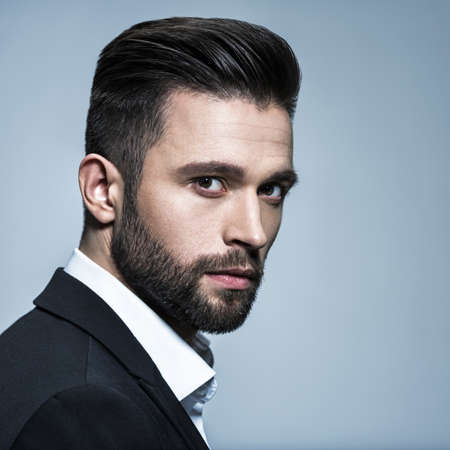 Handsome man in black suit with white shirt  - posing  at studio. Attractive guy with fashion hairstyle.  Confident man with short beard. Adult boy with brown hair.の写真素材