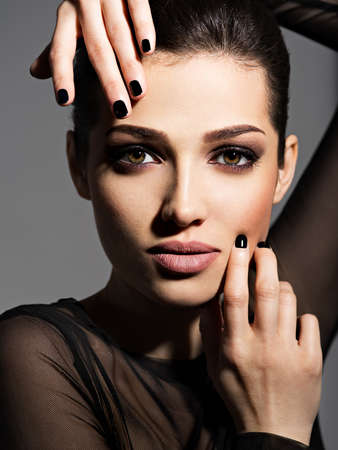 Face of a beautiful girl with fashion makeup and black nails posing at studio over dark background