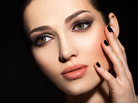 Face of a beautiful girl with fashion makeup and black nails posing at studio over dark background