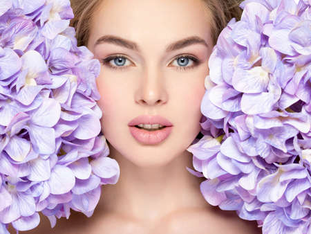 Beautiful young blonde woman with flowers near face -isolated on whiteの写真素材