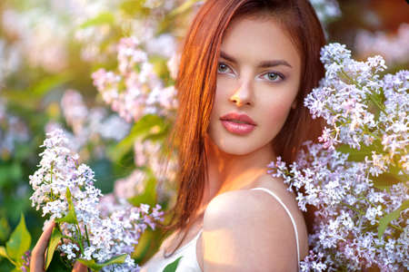 Pretty young woman posing outdoors in nature around her bush of blossoming flowers