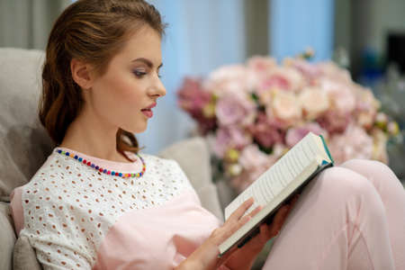 Young attractive woman sitting on the sofa  reading a book enjoys of rest.の写真素材